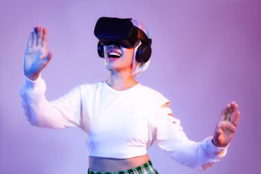 Siyah VR kulaklık takan beyaz tişörtlü mutlu Asyalı kadın mor arka planda oynarken ve el ele tutuşurken izliyor. Metaverse konsepti.