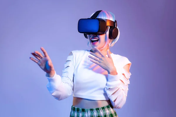 Siyah VR kulaklık takan beyaz tişörtlü genç Asyalı kadın mor arka planda oynarken ve el ele tutuşurken izliyor. Metaverse konsepti.