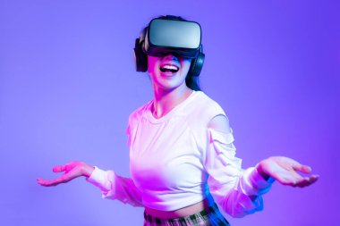 Metaverse konsept, beyaz moda sweatshirt giyen Asyalı genç bir kız VR kulaklık takıyor ve mor arka planda dokunarak ve eğlenerek online oyun oynuyor..