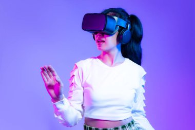 Metaverse concept, young asian girl in white fashion sweatshirt wearing vr headset playing hand touching online game on purple background.