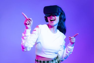 Metaverse konsept, beyaz moda sweatshirt giyen Asyalı genç kız VR kulaklık takıyor ve online oyun mor arka planına dokunuyor..