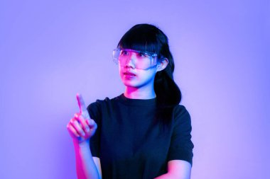Metaverse concept. Young asian woman in black t-shirt wearing vr classes posing touching on purple neon light color background.