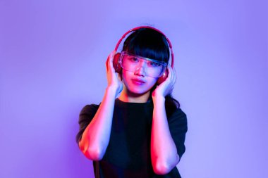 Siyah tişörtlü, gözlüklü, kırmızı kulaklıklı, mor perde arkasında poz veren Asyalı genç kız..