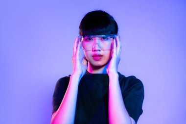 Metaverse concept. Young asian woman in black t-shirt wearing vr classes posing on purple neon light color background.