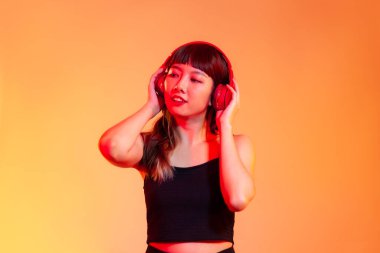 Young asian woman long hair in black tank top wearing red headphones listen to music on the oragne background.