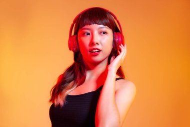 Young asian woman long hair style in black tank top wearing red headphones listen to music on orange background.	