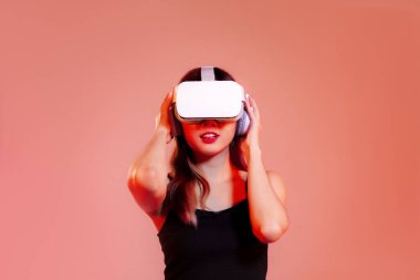 Metaverse konsept, siyah kolsuz bluzlu genç Asyalı kadın VR gözlük takıyor kırmızı pastel arka planda poz veriyor.