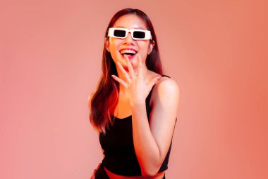 Siyah kolsuz tişörtlü genç Asyalı kadın. Güneş gözlüğü takıyor. Kırmızı ekranda mutlu ve şaşırmış görünüyor.