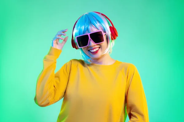 Young asian girl in yellow sweatshirt blue color shot hair style wearing red headphone and pink sunglasses listen to music posing and dancing on the green screen background.