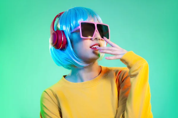 Young asian girl in yellow sweatshirt blue color shot hair style wearing red headphone and pink sunglasses listen to music posing on the green screen background.