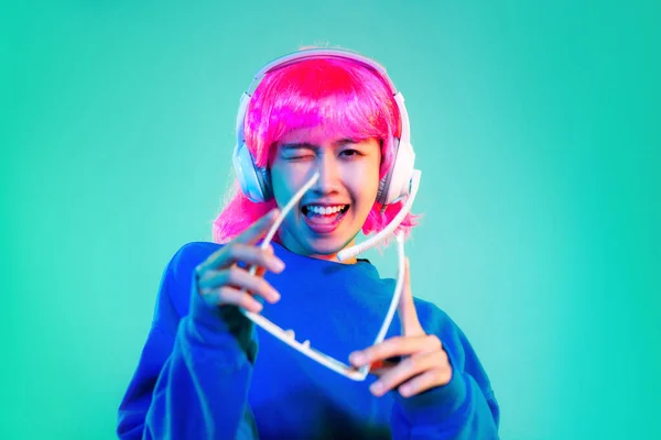 Young asian woman in blue sweatshirt pink short hair punk style wearing sunglasses and headphones posing dancing on the green screen background.