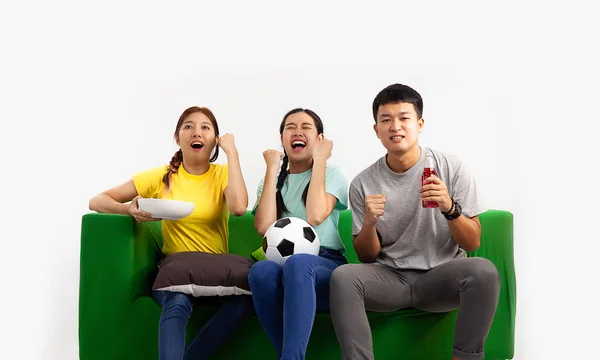 Young asian man and women holding football ball sitting on green sofa watching and cheering the soccer game at home on the white screen background.