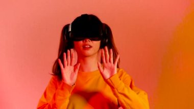 Metaverse concept, young asian woman in orange sweatshirt wearing black vr headset watching playing and touching on the red screen background, 4k video vr woman.
