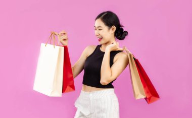 Young asian woman in black tank top hodling colorful paper shopping bags posing on the pink background.