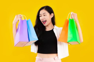Young asian woman long hair style in black and white costume carrying and showing the colorful paper shopping bags on yellow background.