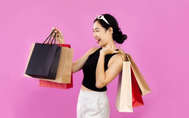 Young asian woman in black crop top carrying and holding paper shopping bags posing on pink background.