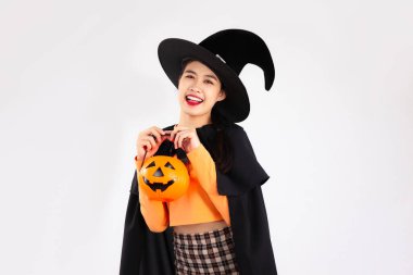 Young asian woman in black clothing wearing witches hat and holding halloween pumpkin on white background to celebrate the Halloween.