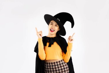 Young asian woman in halloween costume witchcraft and witch hat posing finger pointing for your copy space on white background.