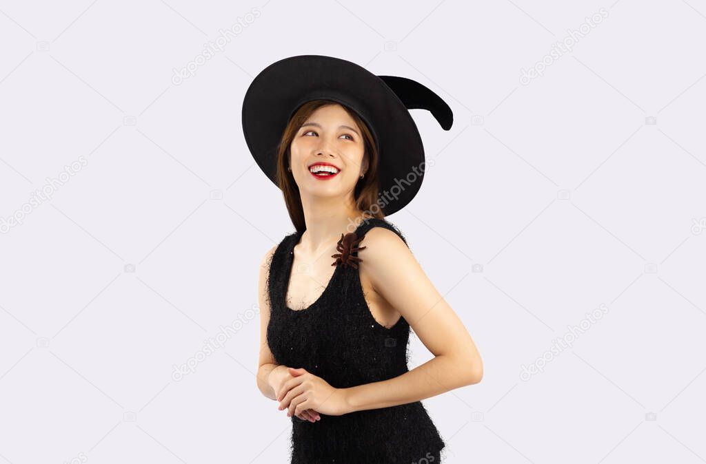 Young asian girl in black dress wearing witch hat to celebrate halloween posing on white background.