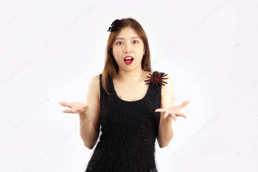 Halloween concept, young asian woman in black dress decorated with black spider posing like a witch on white background.