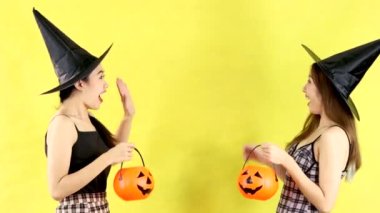 4K video of young asian women in halloween theme wearing witches hat carrying orange pumpkin bucket and lantern playing and moving on yellow background.