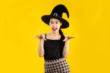 Siyah kolsuz tişörtlü genç Asyalı kadın Cadılar Bayramı konsepti için sarı arka planda poz veriyor..