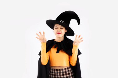 Cadılar Bayramı teması, siyah şapkalı ve büyücülükle beyaz arka planda korkunç poz veren cadı kostümlü genç Asyalı kadın..