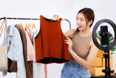 Canlı yayın konsepti, genç Asyalı blogcu kadın akıllı telefon kamerasının önünde kıyafetlerini gösterirken video kaydediyor, canlı sohbet ediyor ve online dükkanında satıyor..