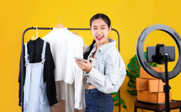 Live streaming concept, young asian blogger woman showing clothes in front of smartphone camera live chatting and selling on her online shop at home.
