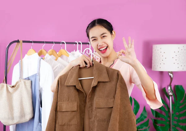 Live streaming and online selling, young asian woman showing clothes in front of smartphone camera while recording vlog video at home.