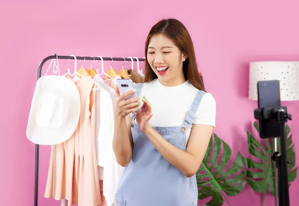 Live streaming, young asian pretty girl using smartphone for marketing online recording vlog video and live streaming at her shop. Pink color room background.
