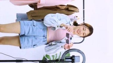 Canlı yayın. 4K video 'da Asyalı genç bir kadın canlı yayında akıllı telefon kamerasının önünde tek gözlü dükkanında sattığı için gözlük gösteriyor. Dikey hikaye videosu.