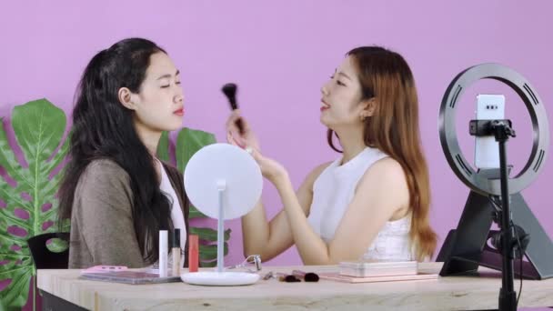 若いアジアのメイクアーティストの女性は ピンク色の背景に彼女のブログを記録しながら スマートフォンのセメラの美しい女性の前で構成する方法をストリーミングライブ 4Kビデオ — ストック動画