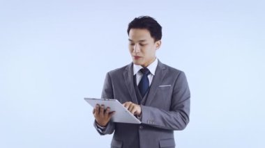 Gri takım elbiseli Asyalı genç bir iş kadını vejetaryen video 4K 'de sohbet ederken tablete dokunuyor. İş konsepti.