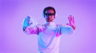 Beyaz kostümlü, video gözlüklü Asyalı bir adam hologram mor arka plana dokunuyor. Metaverse konsept 4K video.