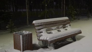 Kış gecesi parkta bir bankta karda bir fenerin ışığında kar yağıyor.