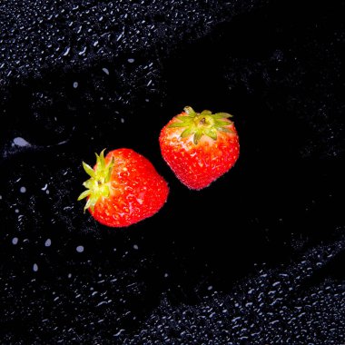Strawberries with water drops on a black background close up, copy space