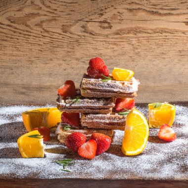 Belçika waffleları marmelat ve çilek, portakal dilimleri, biberiye, eski ahşap bir masaya pudra şekeri serpiştirilmiş, yan görüş, kopyalama alanı, sağlıklı kahvaltı.