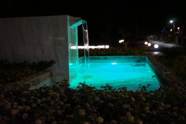 Eylül ayında Lantana Camara 'nın çiçek yataklarıyla çevrili bir çeşme gece aydınlandı. Kolympia, Rodos, Yunanistan 