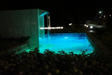 Eylül ayında Lantana Camara 'nın çiçek yataklarıyla çevrili bir çeşme gece aydınlandı. Kolympia, Rodos, Yunanistan 