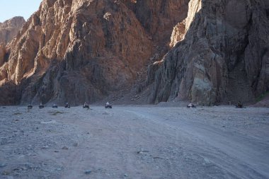 Turistler ATV ile Dahab 'ın pitoresk yerlerinden geçiyorlar. Arazi aracı ATV (ayrıca hafif hizmet aracı LUV, dörtlü bisiklet ya da kısaca Dörtlü bisiklet olarak da bilinir), düşük basınçlı lastikler üzerinde seyahat eden bir araçtır. Dahab, Güney Sina Valiliği, Mısır