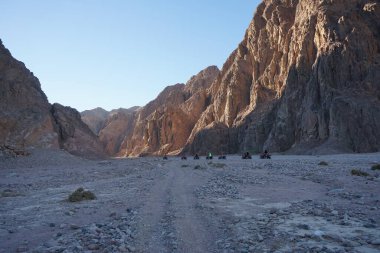 Turistler ATV ile Dahab 'ın pitoresk yerlerinden geçiyorlar. Arazi aracı ATV (ayrıca hafif hizmet aracı LUV, dörtlü bisiklet ya da kısaca Dörtlü bisiklet olarak da bilinir), düşük basınçlı lastikler üzerinde seyahat eden bir araçtır. Dahab, Güney Sina Valiliği, Mısır