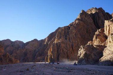 Turistler ATV ile Dahab 'ın pitoresk yerlerinden geçiyorlar. Arazi aracı ATV (ayrıca hafif hizmet aracı LUV, dörtlü bisiklet ya da kısaca Dörtlü bisiklet olarak da bilinir), düşük basınçlı lastikler üzerinde seyahat eden bir araçtır. Dahab, Güney Sina Valiliği, Mısır