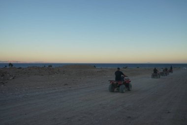 Turistler ATV ile Dahab 'ın pitoresk yerlerinden geçiyorlar. Arazi aracı ATV (ayrıca hafif hizmet aracı LUV, dörtlü bisiklet ya da kısaca Dörtlü bisiklet olarak da bilinir), düşük basınçlı lastikler üzerinde seyahat eden bir araçtır. Dahab, Güney Sina Valiliği, Mısır