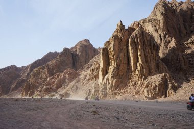 Turistler ATV ile Dahab 'ın pitoresk yerlerinden geçiyorlar. Arazi aracı ATV (ayrıca hafif hizmet aracı LUV, dörtlü bisiklet ya da kısaca kuad olarak da bilinir) bir araçtır. Dahab. 