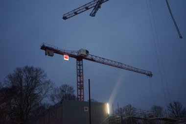 Akşam gökyüzünün arka planına karşı çalışan vinçler. Vinç genellikle kaldırma halatı, tel halatlar, zincirler ve demetler ile donatılmış bir makinedir, hem kaldırma hem de alttaki malzemeleri yatay olarak hareket ettirmek için kullanılabilir. Berlin