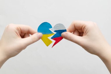 Ukrayna 'daki savaşı bitirme kavramı. Ukrayna ve Rusya bayrağının renginde kırık bir kalp kadınların elinde.