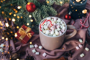 Marşmelovlu kakao kupası, köknar dalları, Noel ışıkları ve pembe tekstil arka planında bir kutuda hediye. Noel, kış tatili konsepti. Üst görünüm.