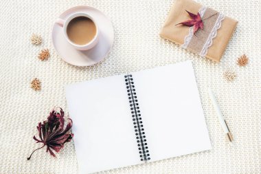 Boş not defteri, kahve fincanı, bir kutuda hediye beyaz örülü ekose arka planda kalem ve sonbahar yaprakları. Üst manzara, düz yatış. Sonbahar kavramı