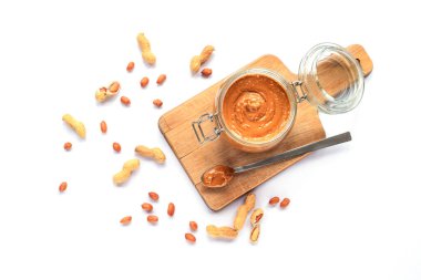 Tahta kesme tahtasındaki kavanozda fıstık ezmesi, beyaz arka planda izole edilmiş fıstıklar. Vejetaryen yemeği. Üst görünüm, düz görünüm, kopyalama alanı.